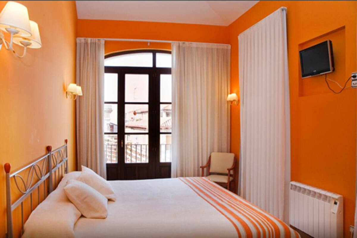 Ett hotellrum med en stor säng, en stol, en tv och ett fönster med gardiner.