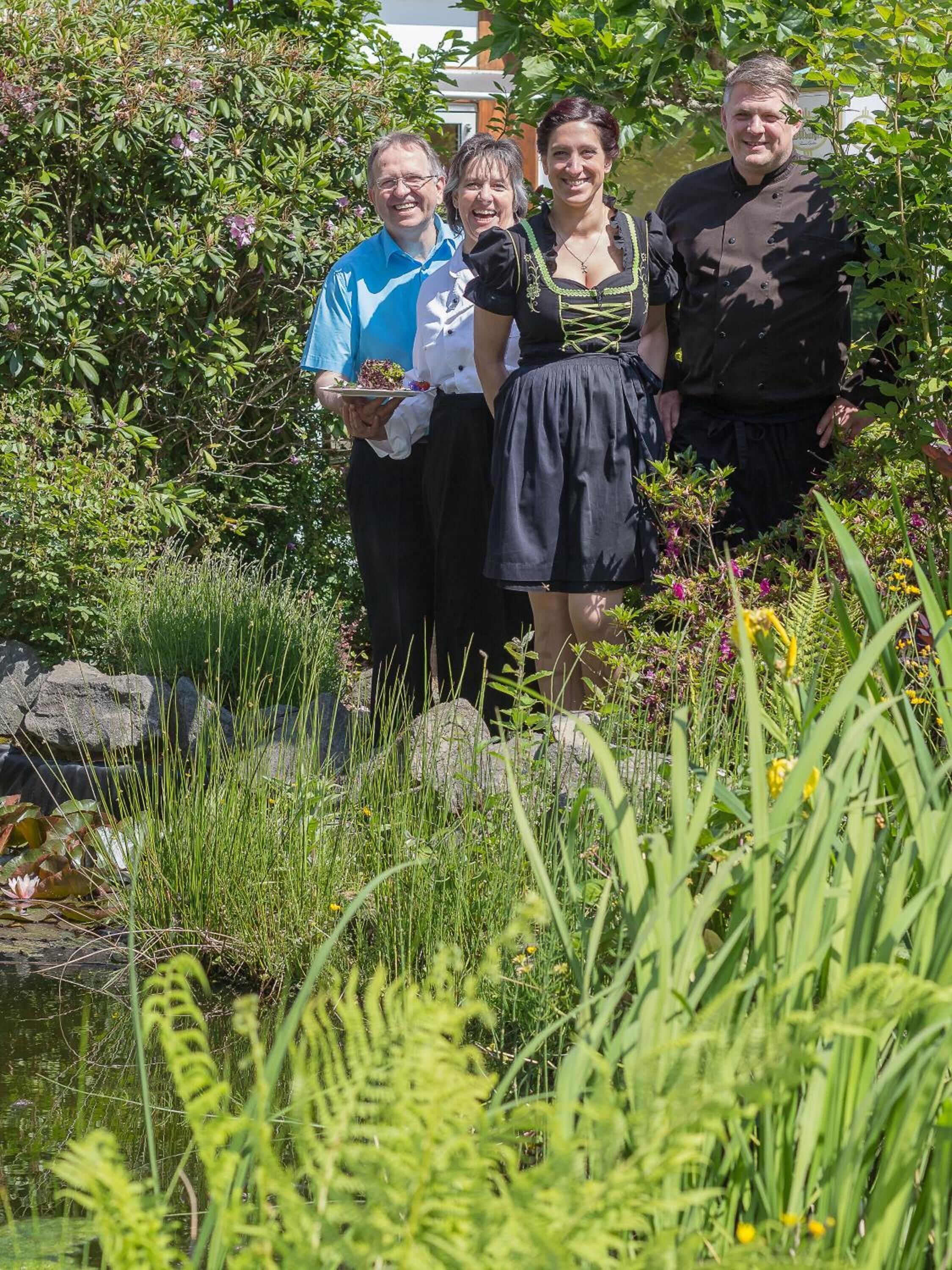 Een groep mensen staat in een tuin met een vijver en verschillende planten.