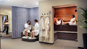 Un espace spa moderne avec un banc en bois, un miroir et un mur orné d’un motif d’arbre.