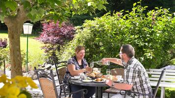 Un espace extérieur aménagé pour les repas, avec une table ronde, des chaises en osier et un banc.