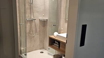 A modern bathroom with a glass-enclosed shower, a white sink, and a marble-tiled floor.