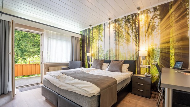 Une chambre moderne avec un grand lit, un bureau et une vue sur une forêt par la fenêtre.