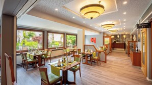 Un restaurant doté de nombreuses tables et chaises, de grandes fenêtres donnant sur l’extérieur et d’un panneau indiquant l’emplacement des toilettes.