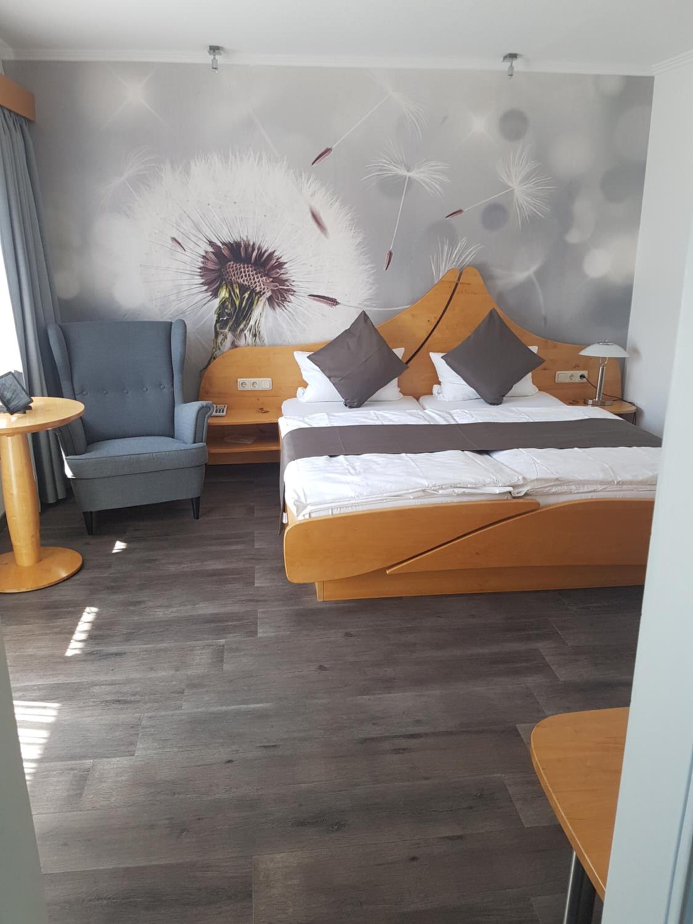 A hotel room with a bed, a chair, a small table, and a wall with a floral mural.