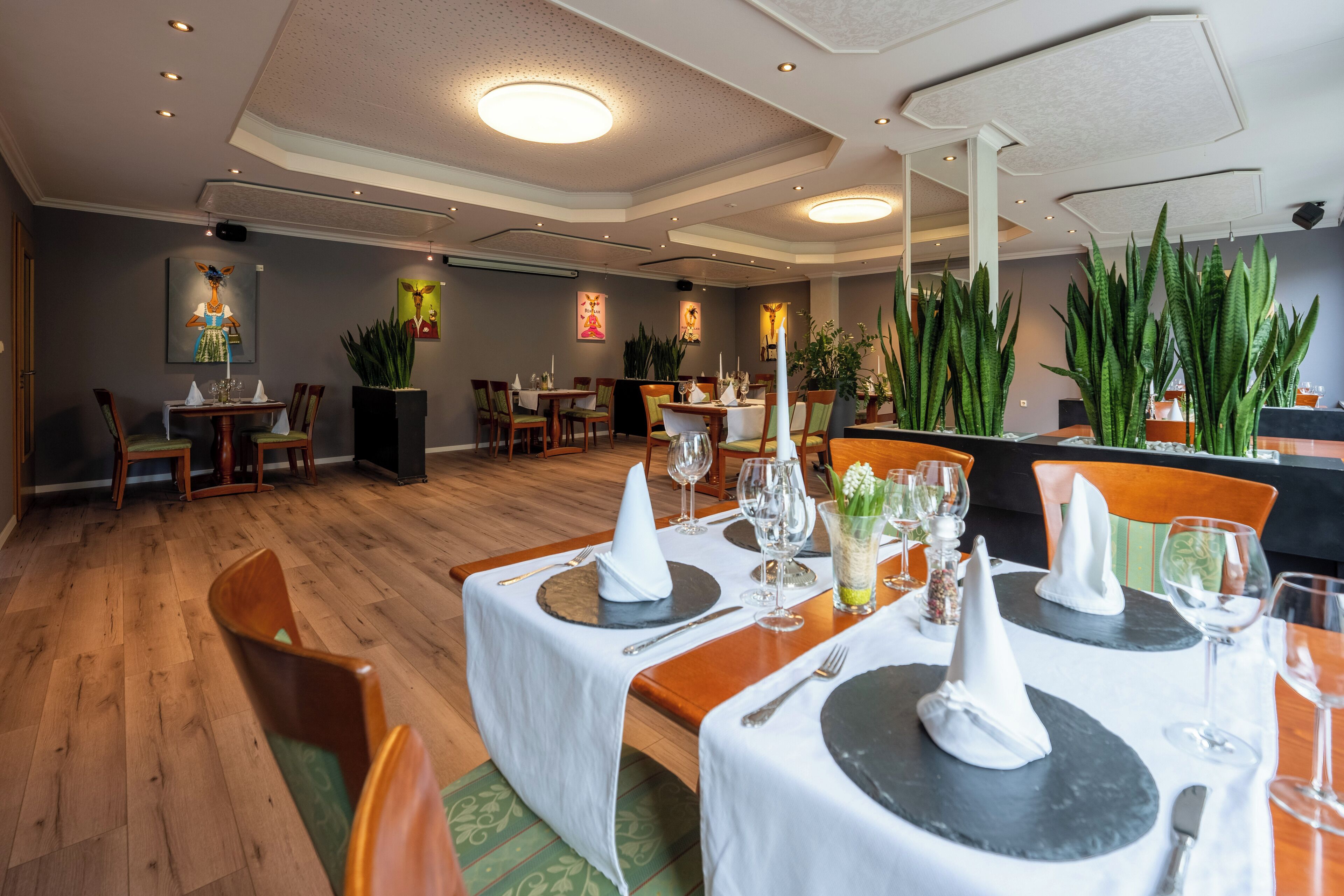 A restaurant with wooden flooring, round tables with white tablecloths, and green chairs.