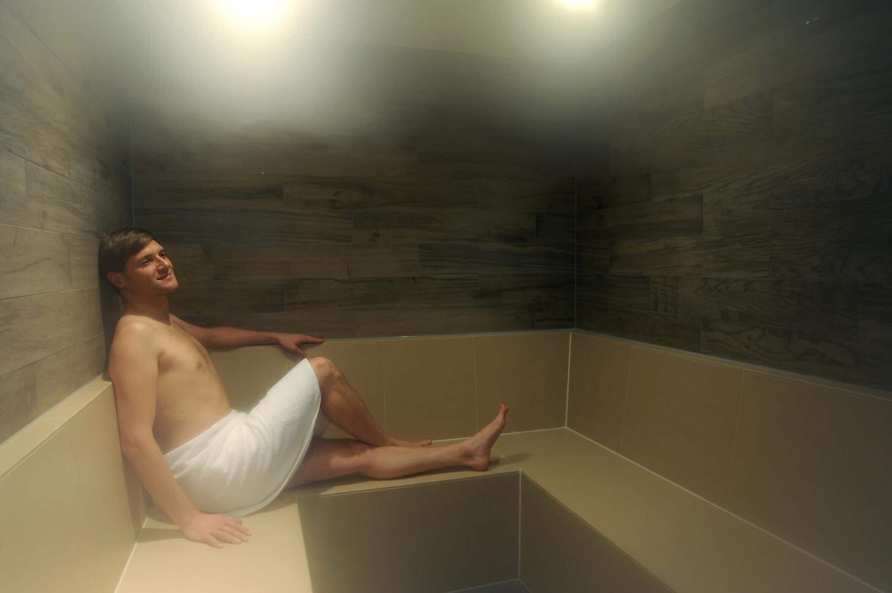 Une personne assise dans une baignoire dont les parois sont en bois et le sol carrelé.