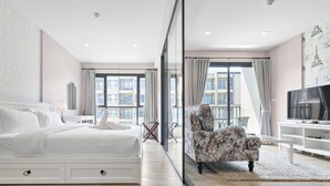 Ein modernes Hotelzimmer mit einem großen Bett, einer Couch, einem Fernseher und Blick auf die Stadt durch große Fenster.