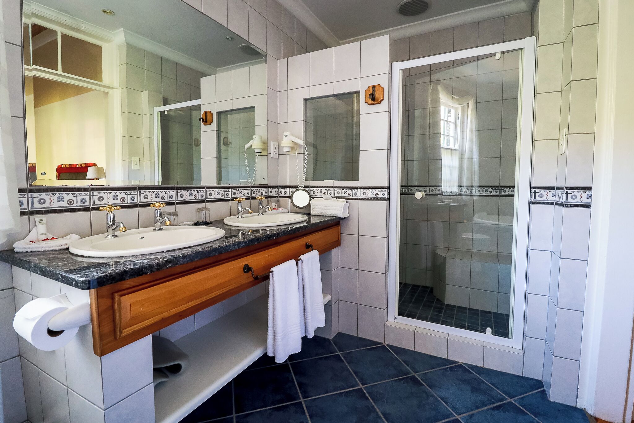 A bathroom with two sinks, a mirror, a towel rack, and a shower area.
