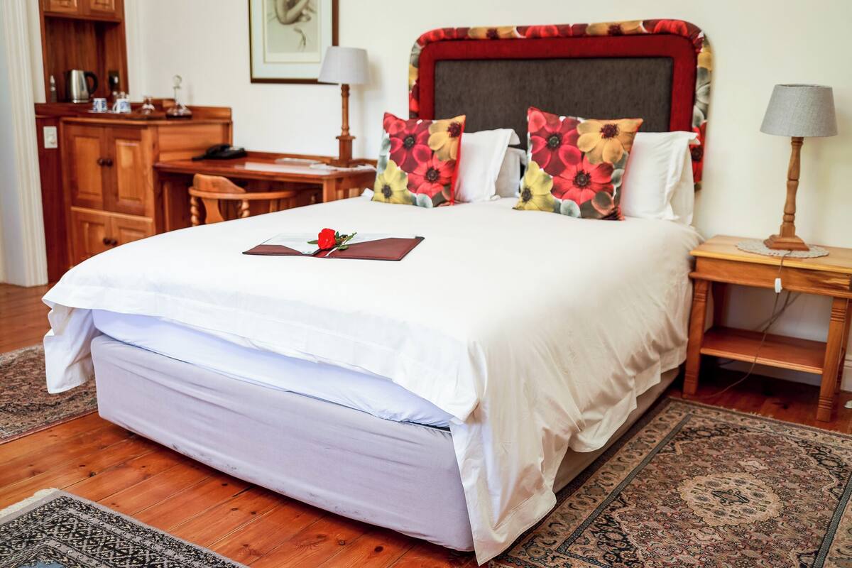 A neatly made bed with a red rose, wooden headboard, and floral pillows.