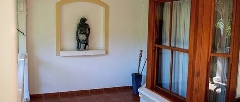 A room with a tiled floor, a statue on a shelf, a window with curtains, and a wooden cabinet.
