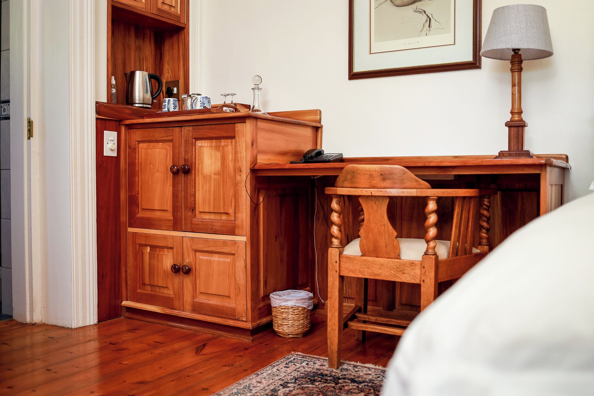 Ein Holzschrank mit Telefon, Lampe und einem gerahmten Bild an der Wand.