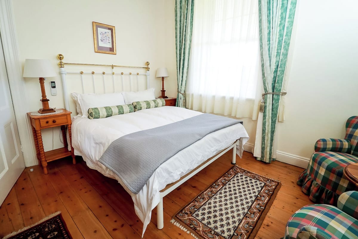A neatly arranged bedroom with a bed, bedside tables, a chair, and a patterned rug.