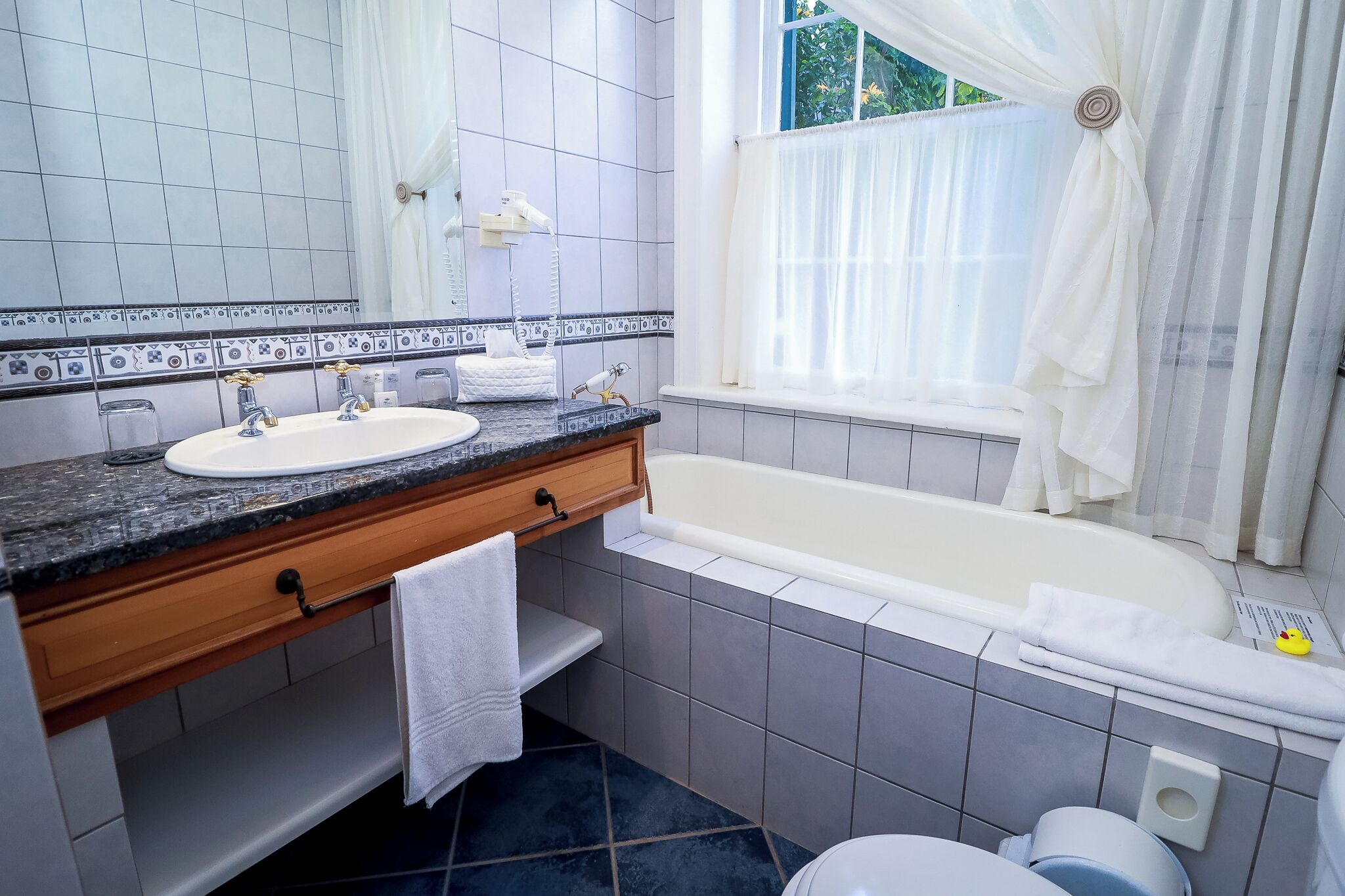 A bathroom with a double sink, vanity, bathtub, and a window with curtains.