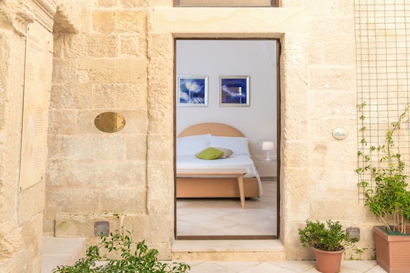 A stone-walled room with a bed, two framed pictures on the wall, and potted plants.