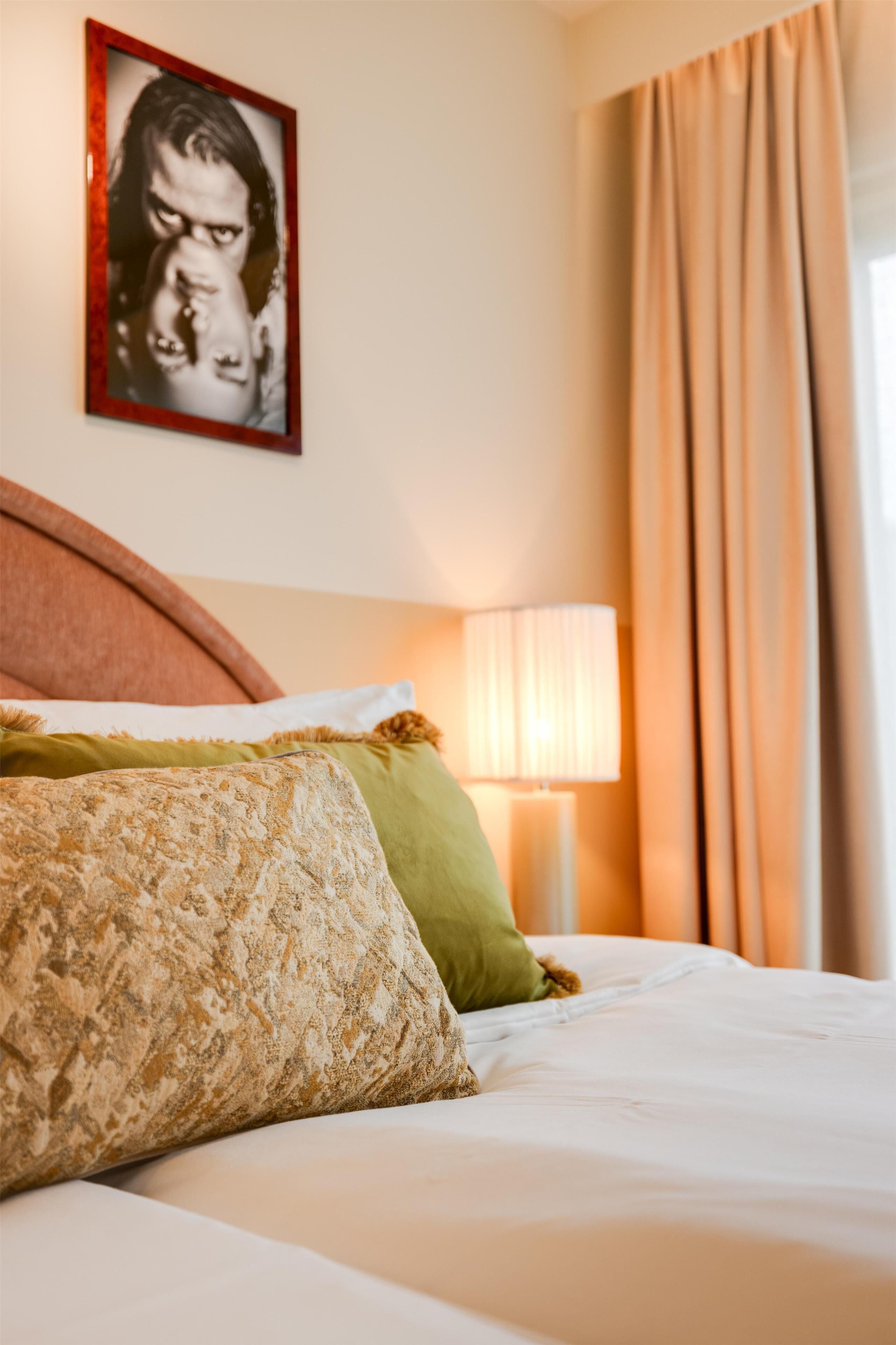 Ein Hotelzimmer mit Bett, Kissen, einer Lampe und einem gerahmten Bild an der Wand.