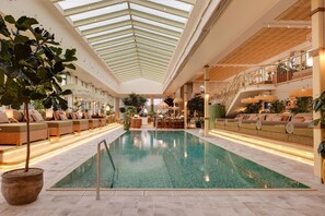 Una piscina interior con techo de vidrio, zonas de estar y plantas.