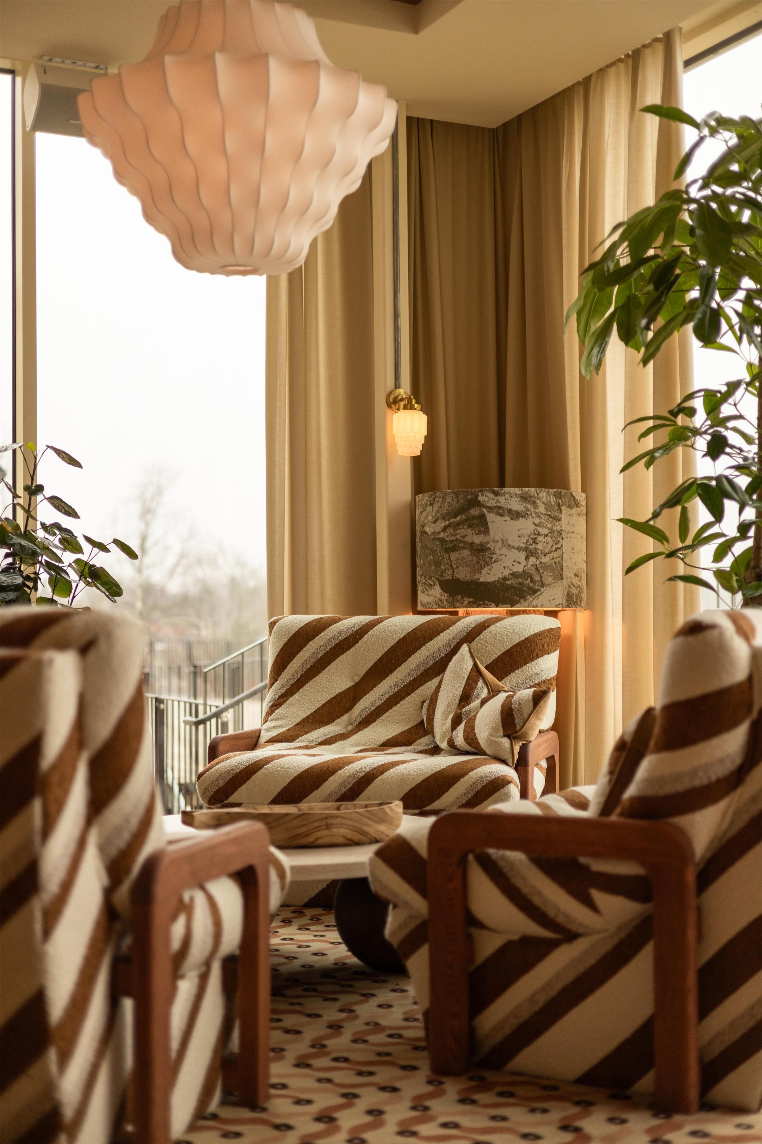 A cozy living room with striped armchairs, a sofa, a decorative lamp, and a view of the outdoors.