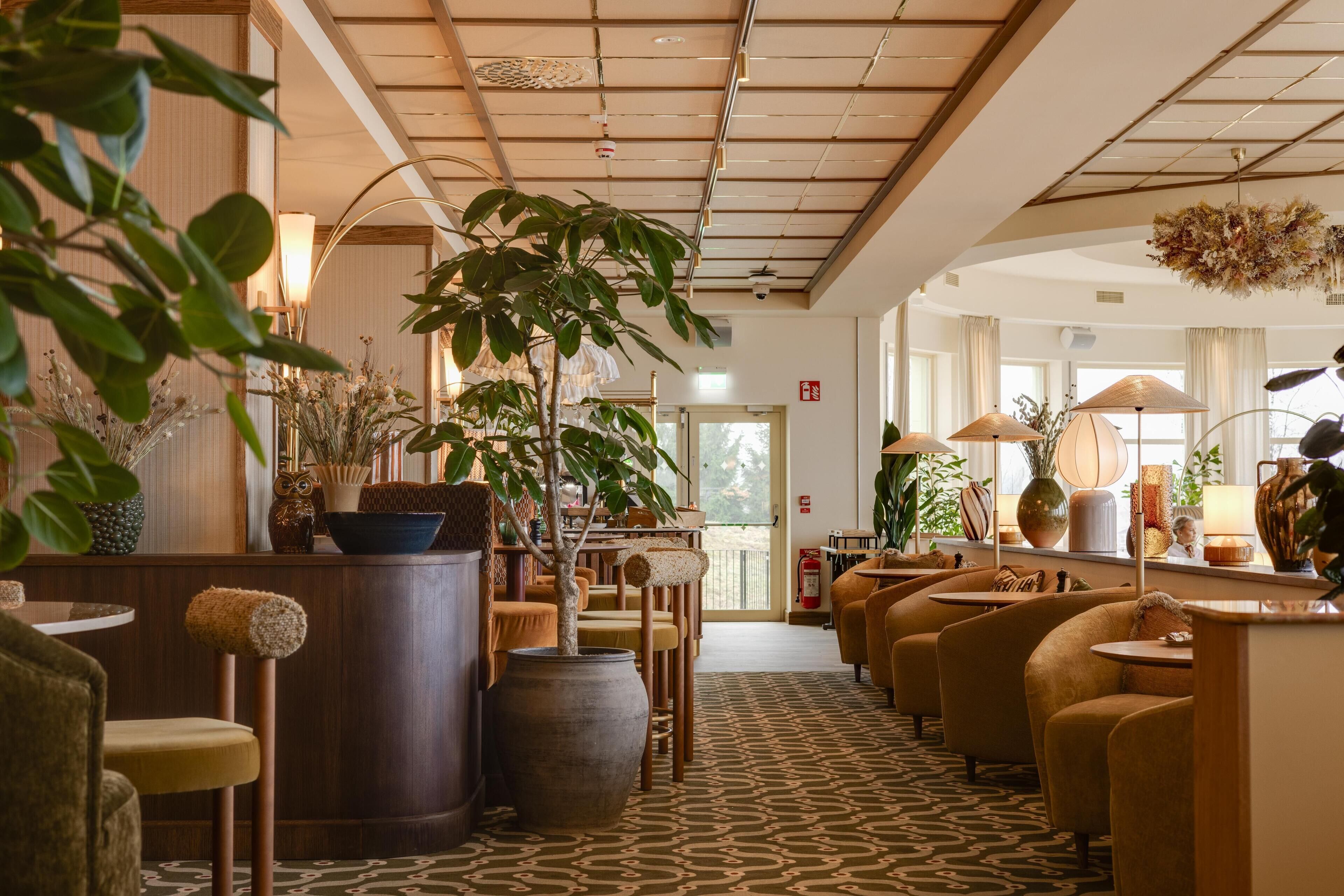 Una hall d'albergo con un'area salotto centrale, grandi piante in vaso e una tappezzeria decorata.