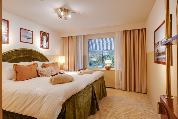 Una habitación de hotel con una cama grande, una ventana con cortinas, un ventilador de techo y cuadros en la pared.