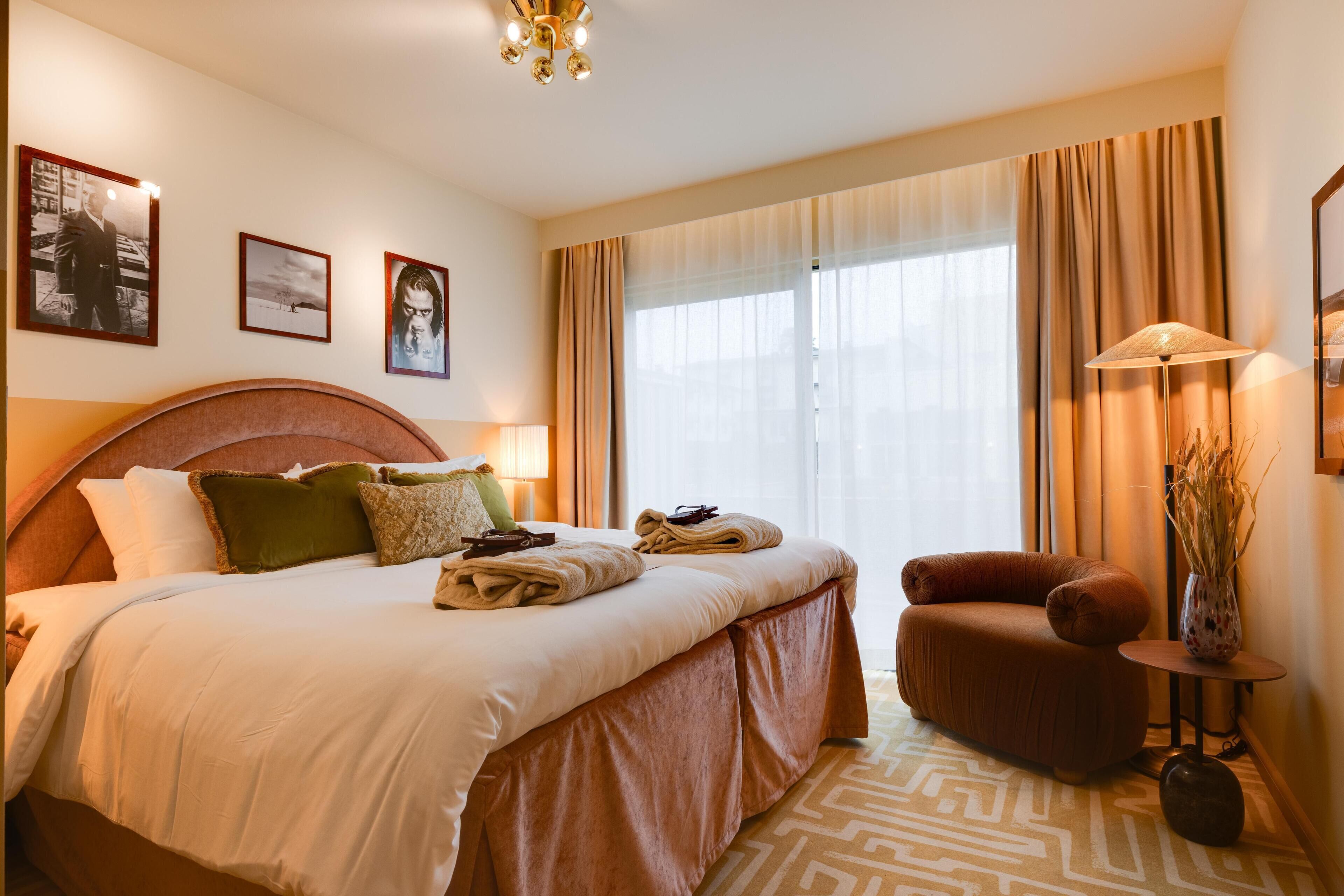 Quarto de hotel com uma cama grande, um sofá, um abajur e um vaso com plantas.
