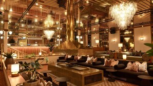 Eine moderne Hotellobby mit einer zentralen Sitzecke, einer Bar und einer Treppe zu einer oberen Ebene.
