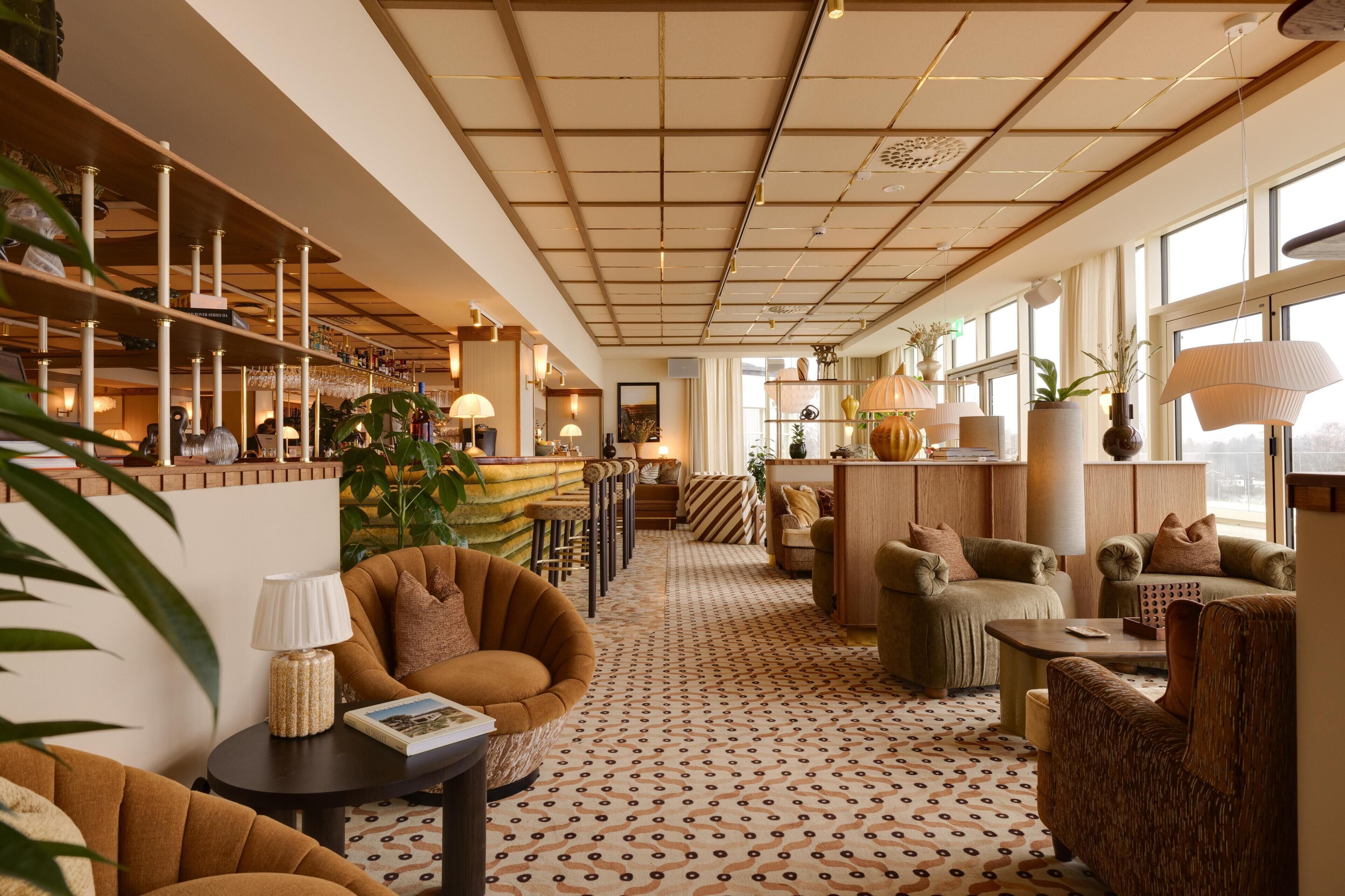 Een ruime zithoek met een vloer in een patroon, comfortabele zitplaatsen en een bar met planken en planten.