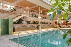 A spacious indoor swimming pool with a sunlit atrium, multiple levels with seating, and a variety of plants. - Hjortviken Country Club (Hindas)