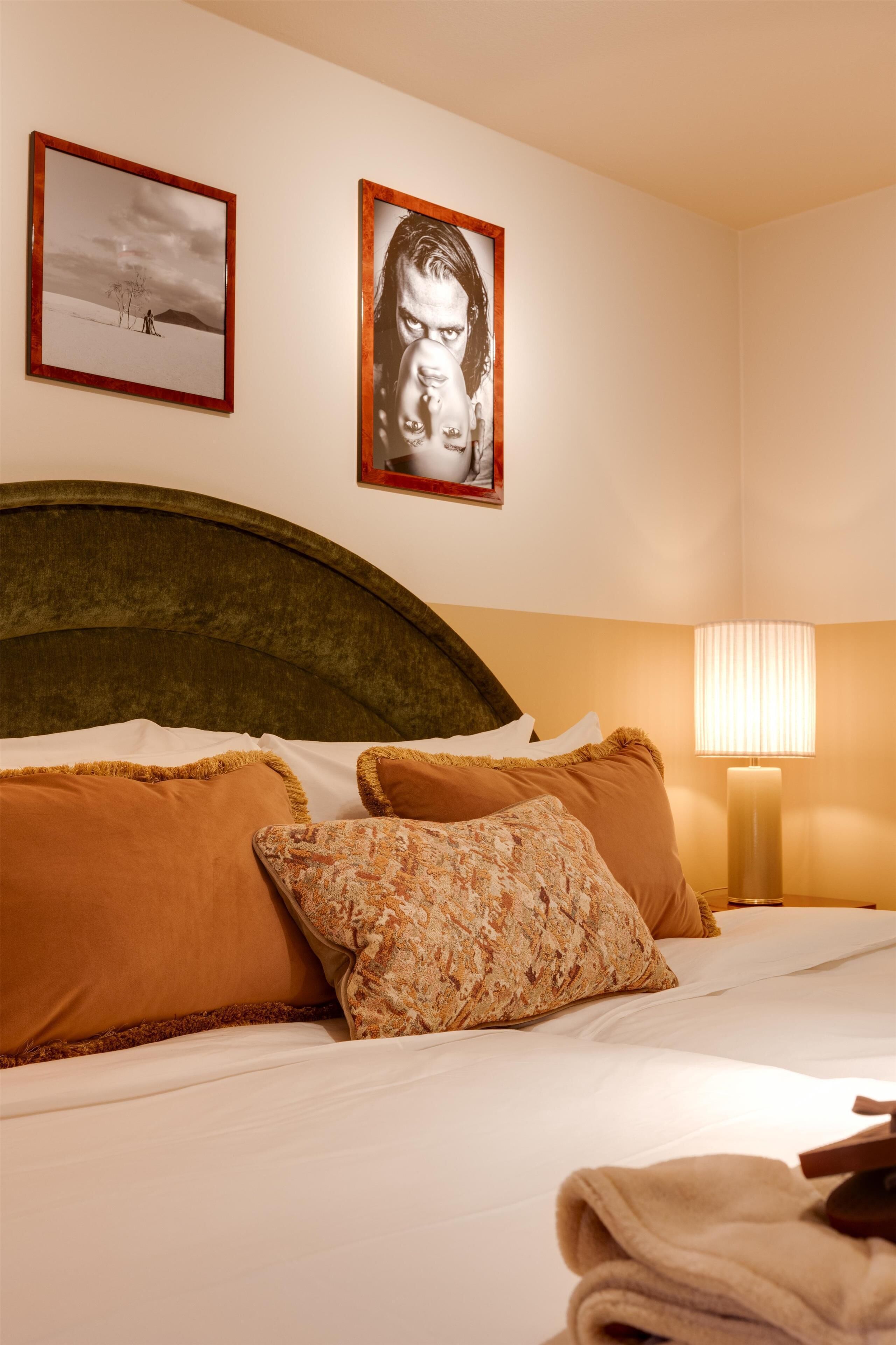 Una cama bien hecha con almohadas marrones y estampadas, un cabecero y dos cuadros en la pared.