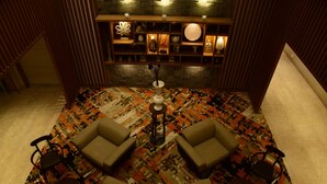 A room with a patterned carpet, a central table with a vase, and a shelving unit with decorative items. - Lemon Tree Hotel Siliguri (Jalpaiguri)