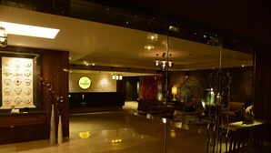 A spacious lobby with a reception desk, a wall of decorative masks, and a seating area with a red curtain backdrop. - Lemon Tree Hotel Siliguri (Jalpaiguri)