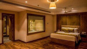 A bedroom with a large window, a bed, a ceiling fan, and a nightstand. - Lemon Tree Hotel Siliguri (Jalpaiguri)