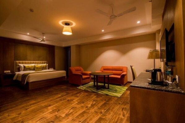 Habitación de hotel con cama, dos sillones, una mesita, ventilador de techo y zona de kitchenette.