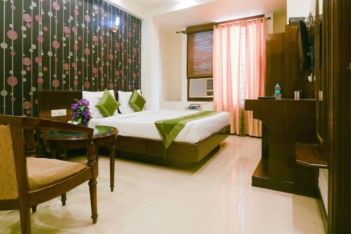 A hotel room with a bed, a chair, a small table with a vase of flowers, and a wooden desk.
