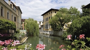 A canal with buildings on either side, surrounded by greenery and flowers.