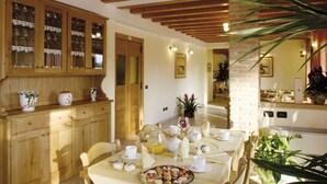 A dining area with a table set for two, wooden chairs, a buffet cabinet with glass doors, and a potted plant.