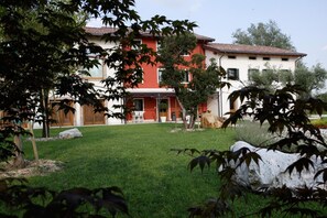 Un edificio de dos pisos con fachada roja y blanca, un patio cubierto de césped y un muro de piedra al frente.