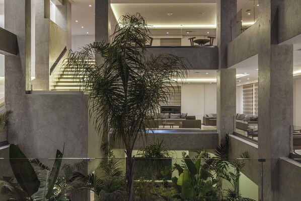 A multi-level interior with a central staircase, a pool area, and a variety of indoor plants. - Ostria Resort & Spa (Ierapetra)
