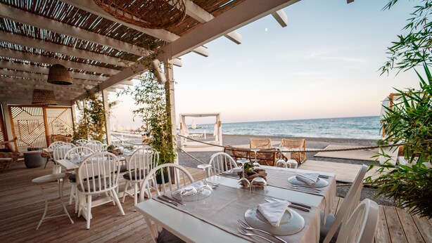 An outdoor dining area with white tables and chairs, overlooking the beach. - Ostria Resort & Spa (Ierapetra)