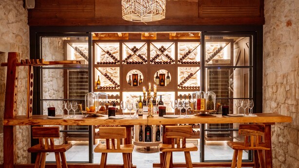 Un comptoir en bois avec une étagère à bouteilles derrière, plusieurs bouteilles, des verres et un chandelier.