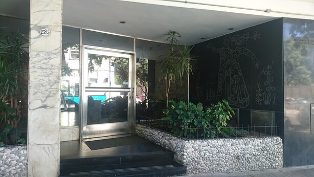 A building entrance with a marble column, a glass door, and a stone wall with plants. - Palermo Open View (Buenos Aires)