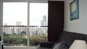 A living room with a grey sofa, a table lamp, and a view of a cityscape through a large window. - Palermo Open View (Buenos Aires)