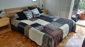 A bedroom with a wooden bed, a nightstand, a lamp, and a window with a view of greenery. - Palermo Open View (Buenos Aires)