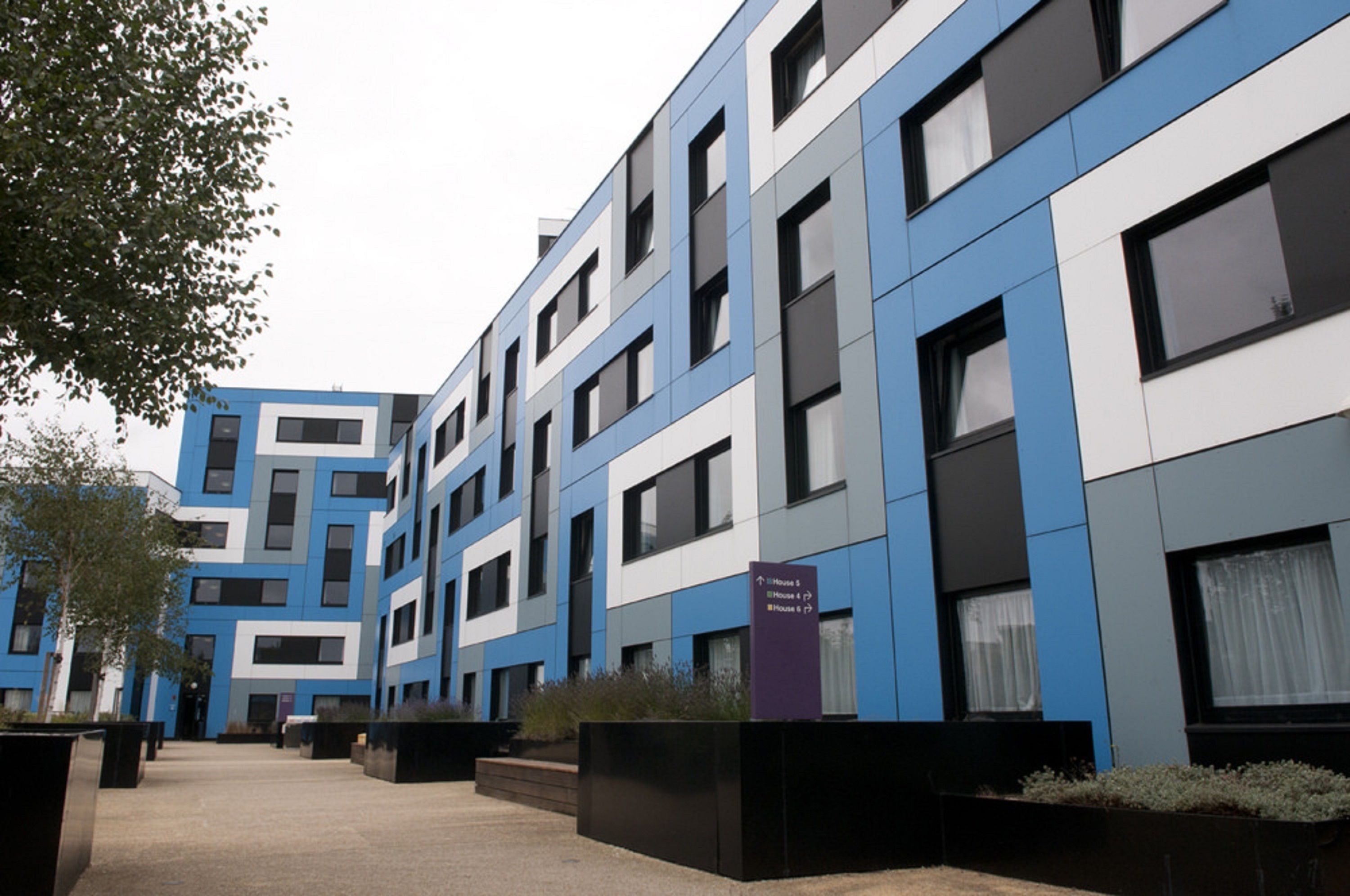 A modern multi-story building with a blue and white facade, multiple windows, and a sign indicating room numbers.