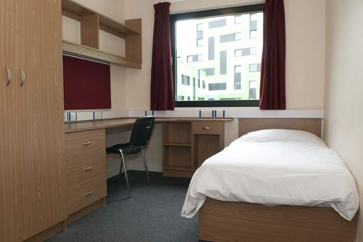 Une petite chambre comprenant un lit, un bureau, une chaise et une armoire.