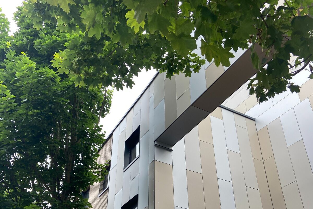 A modern building with a flat roof and a facade featuring a mix of beige and gray panels.