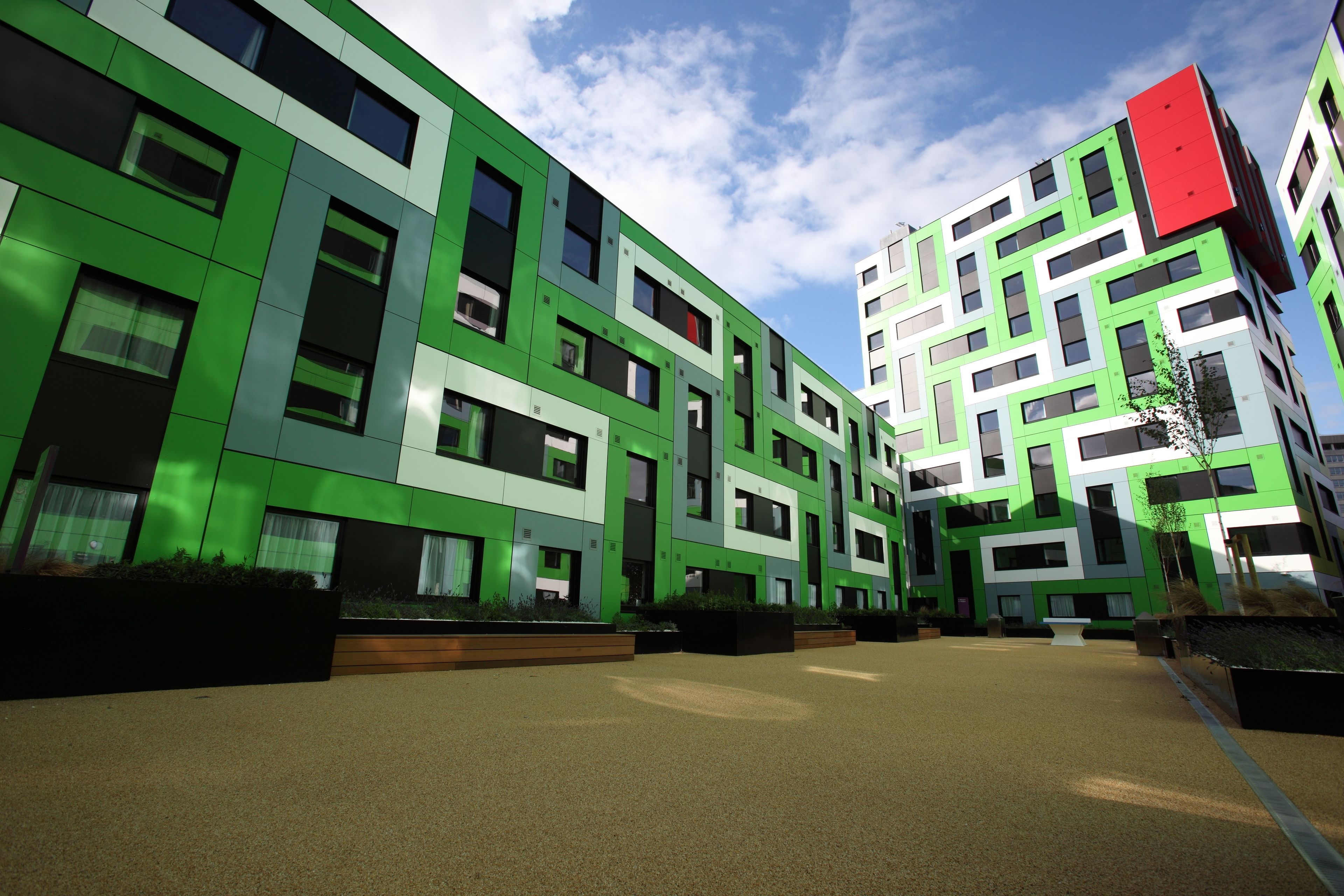 A modern building with a green facade, multiple windows, and a courtyard with seating areas.
