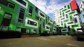 A modern building with a green facade, multiple windows, and a courtyard with seating areas.