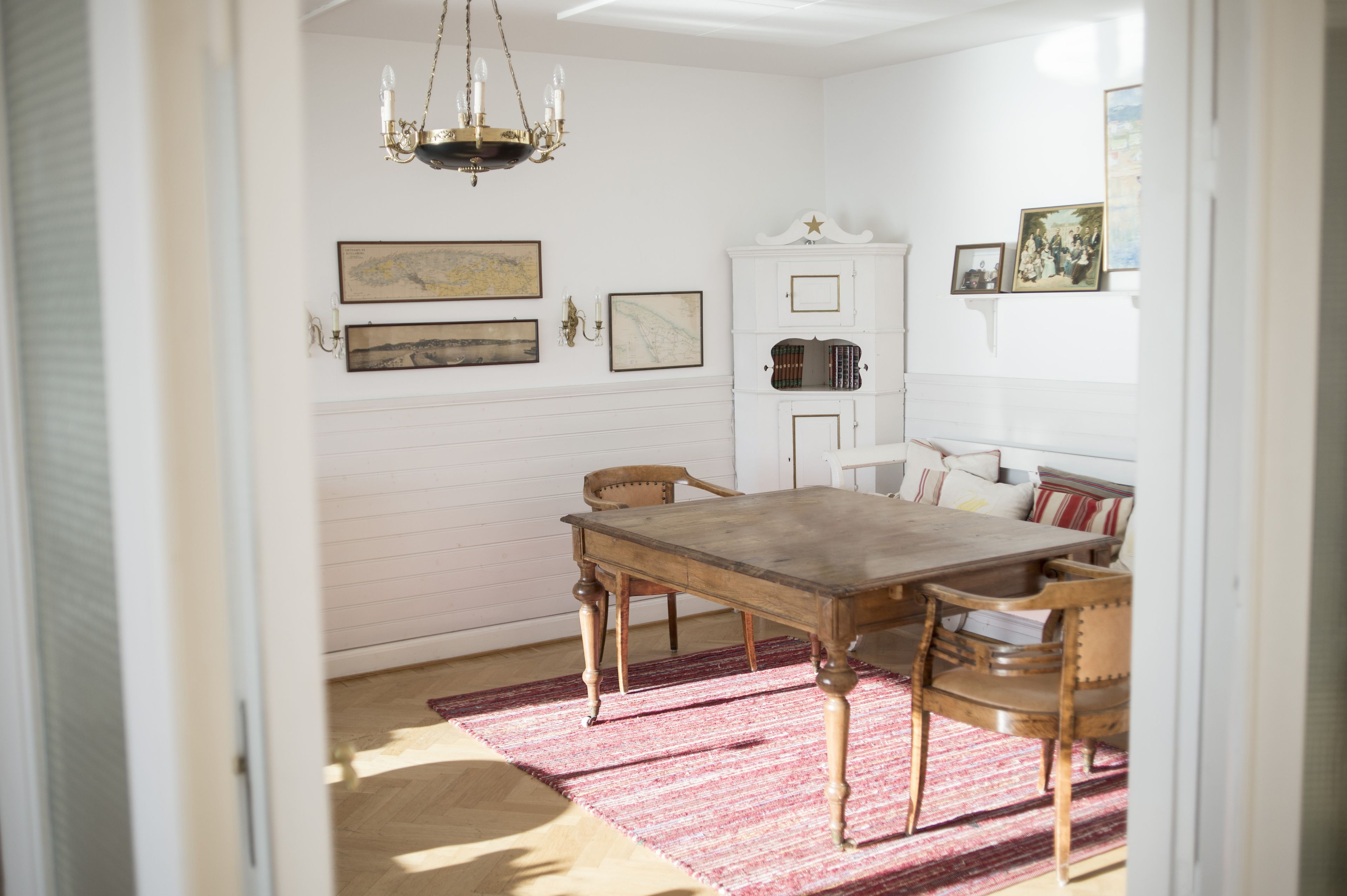 A dining room with a wooden table, chairs, a chandelier, and a red rug.