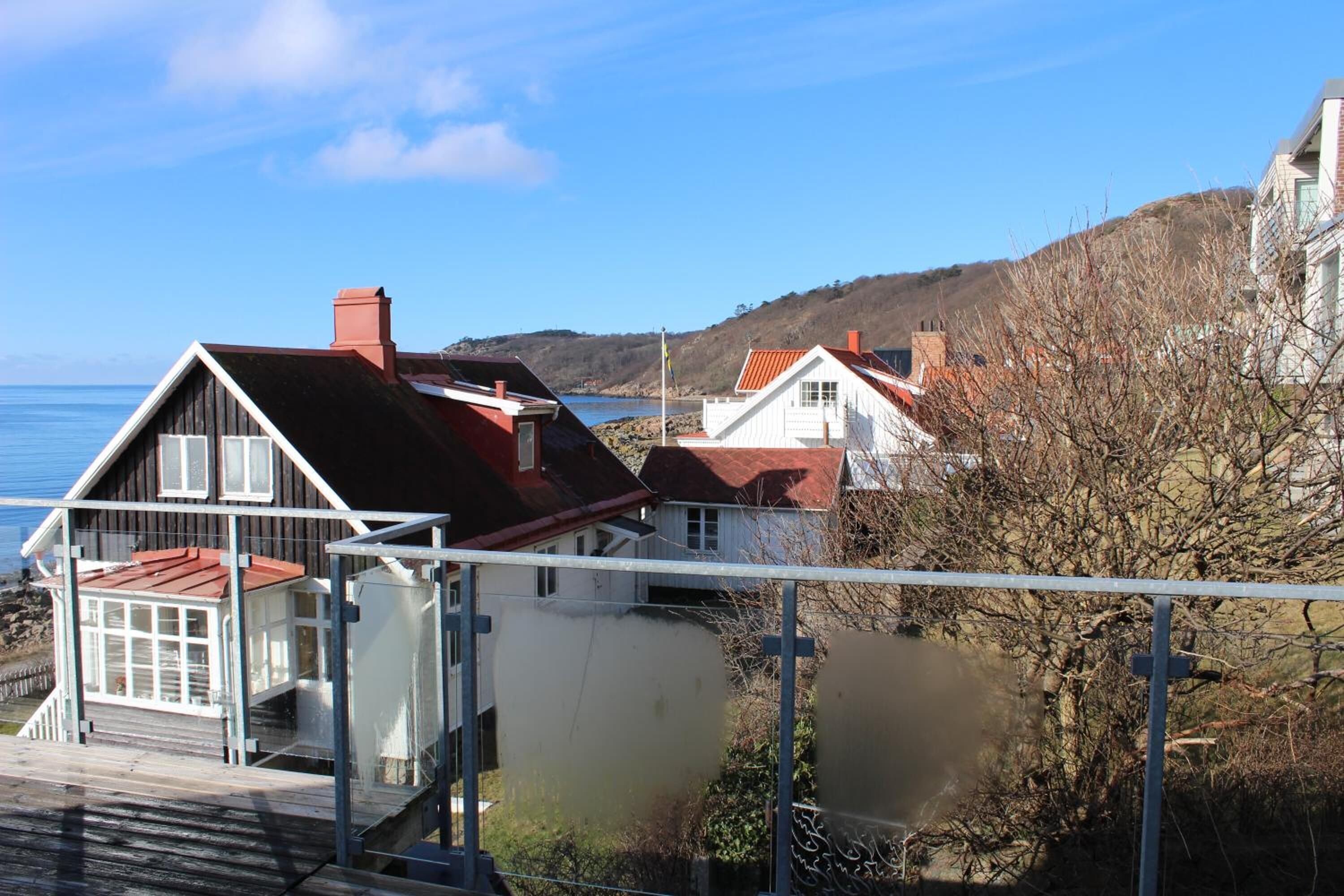 A coastal house with a red roof, white walls, and a balcony overlooking the sea.