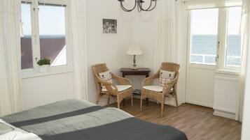 Une chambre à coucher avec un lit, deux fauteuils en osier, une petite table, une lampe et un tableau au mur.